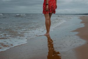 Frau die am Wasser stehht und Füße ins Meer hält